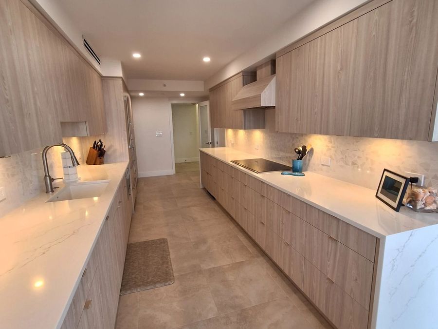 Completed galley kitchen with light wood cabinets, white counters, and under-cabinet lighting